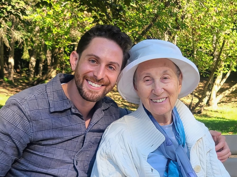 Moshe Birnbaum smiling beside his grandmother on a park bench