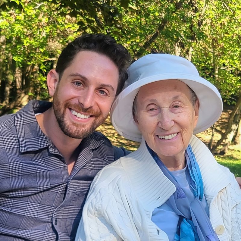 Moshe Birnbaum and his grandmother, in a white sun hat, smiling together outdoors